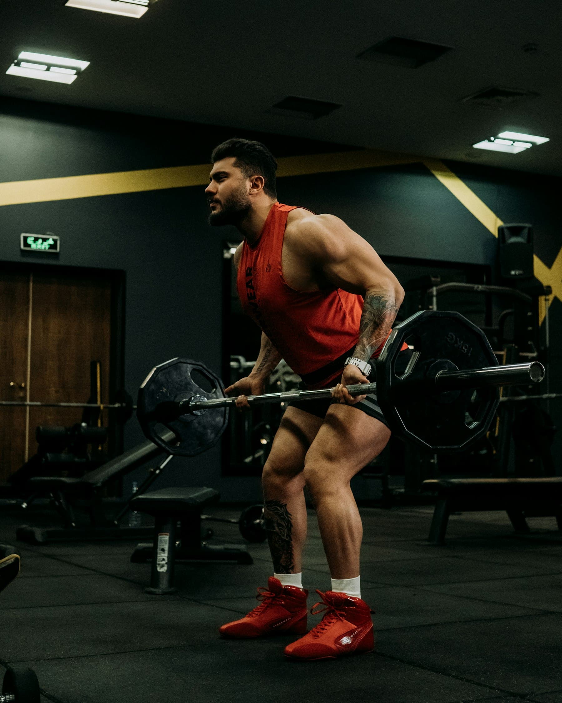 A man setting up a heavy barbell lift in a dark, well-equipped gym