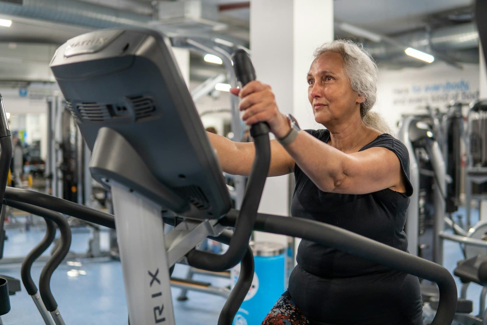 An older woman working out on a cross-trainer at a gym